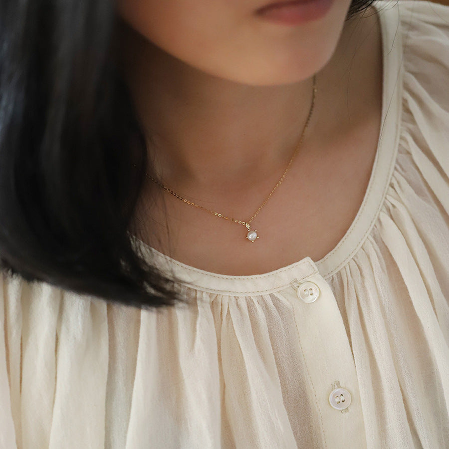 Close-up of a person wearing a delicate gold necklace with a small pendant.