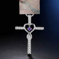Silver cross pendant with heart design and purple gemstone on a dark background