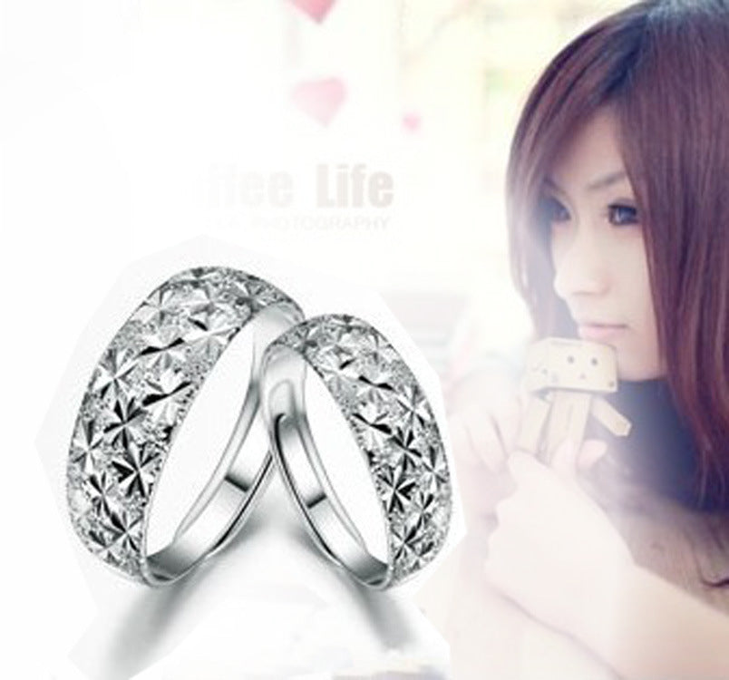 Two silver rings with clear stones on a white background, with a blurred woman in the background.