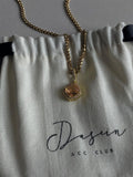 Gold necklace with a pendant on a Dasein ACC Club branded pouch.