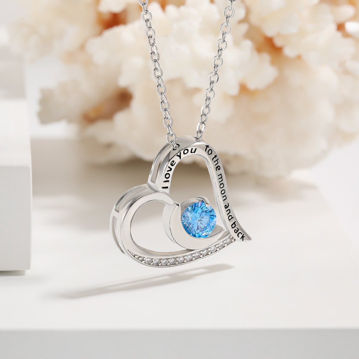 Silver heart-shaped necklace with a blue gemstone on a white background