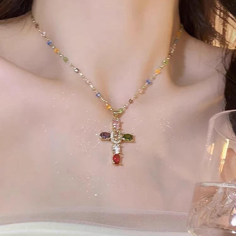 Necklace with a cross pendant featuring multicolored gemstones on a plain background