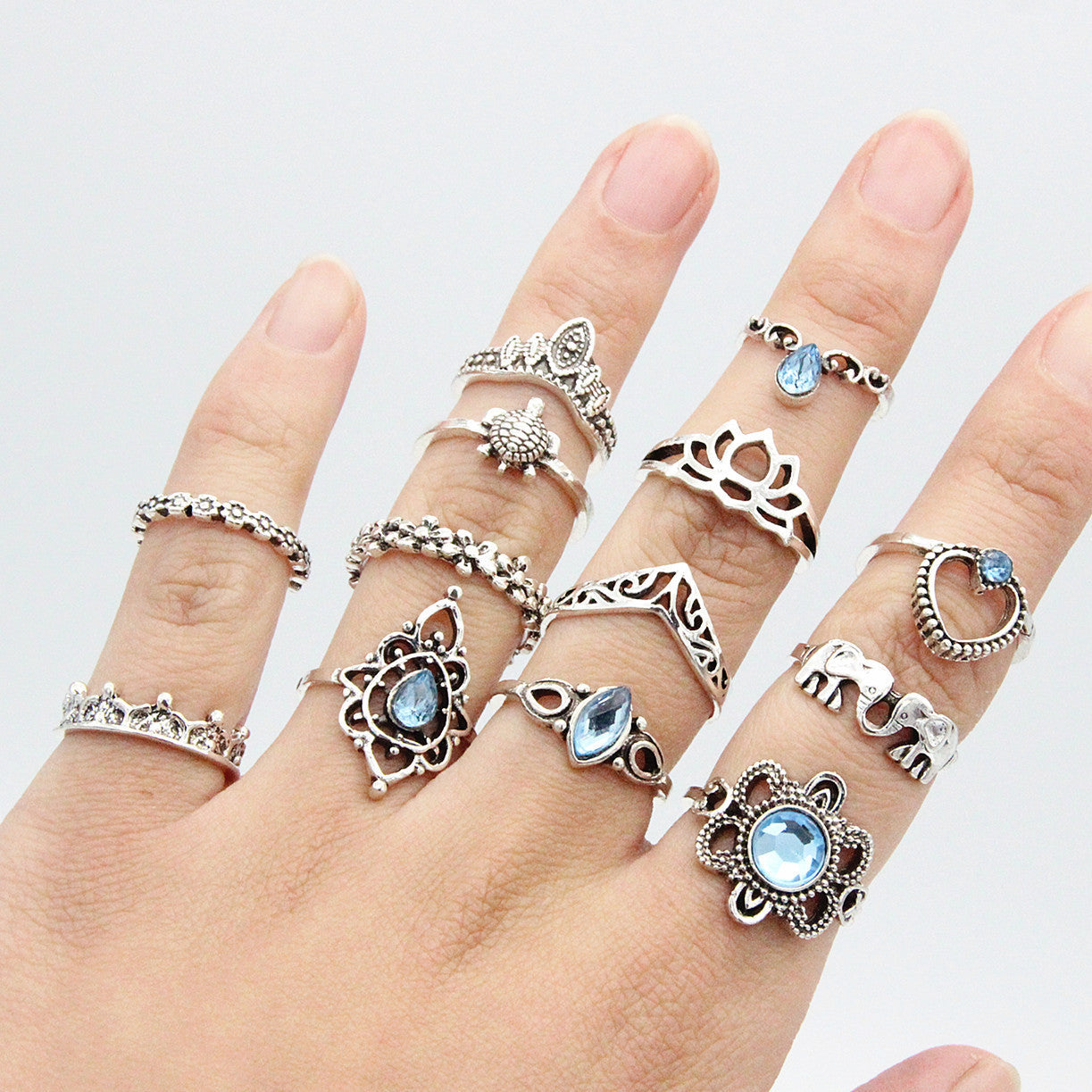 Hand wearing multiple silver rings with gemstones on a white background