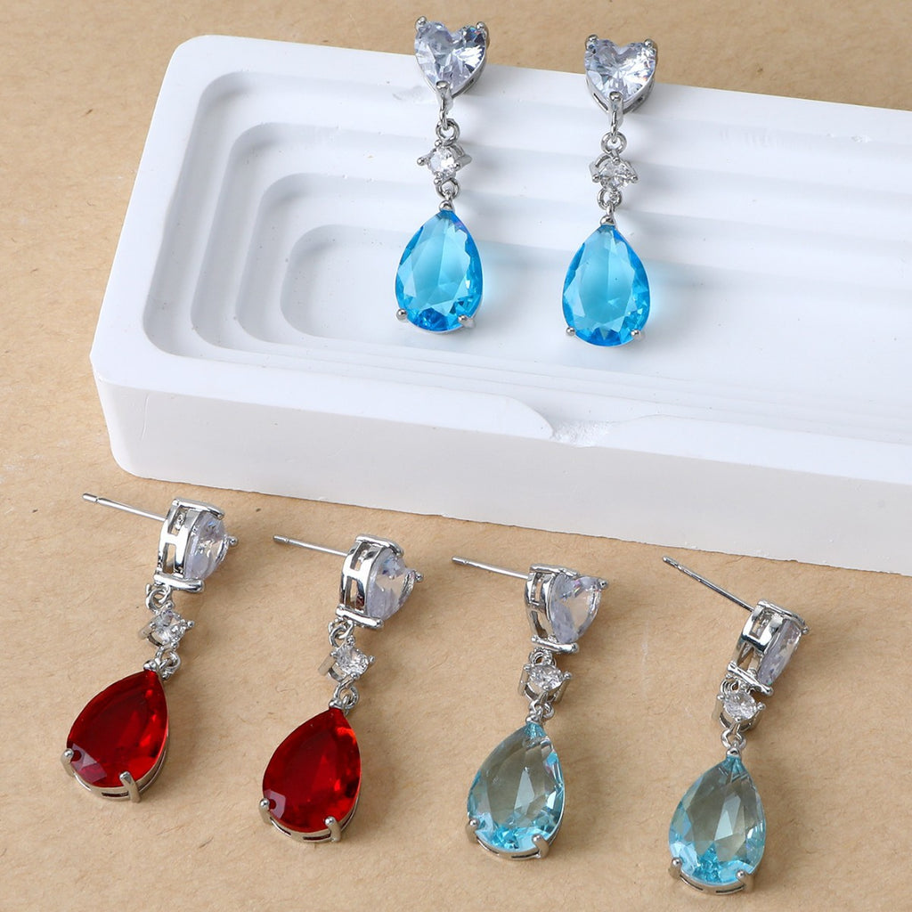 Pair of blue teardrop earrings on a white stand with additional pairs displayed below.