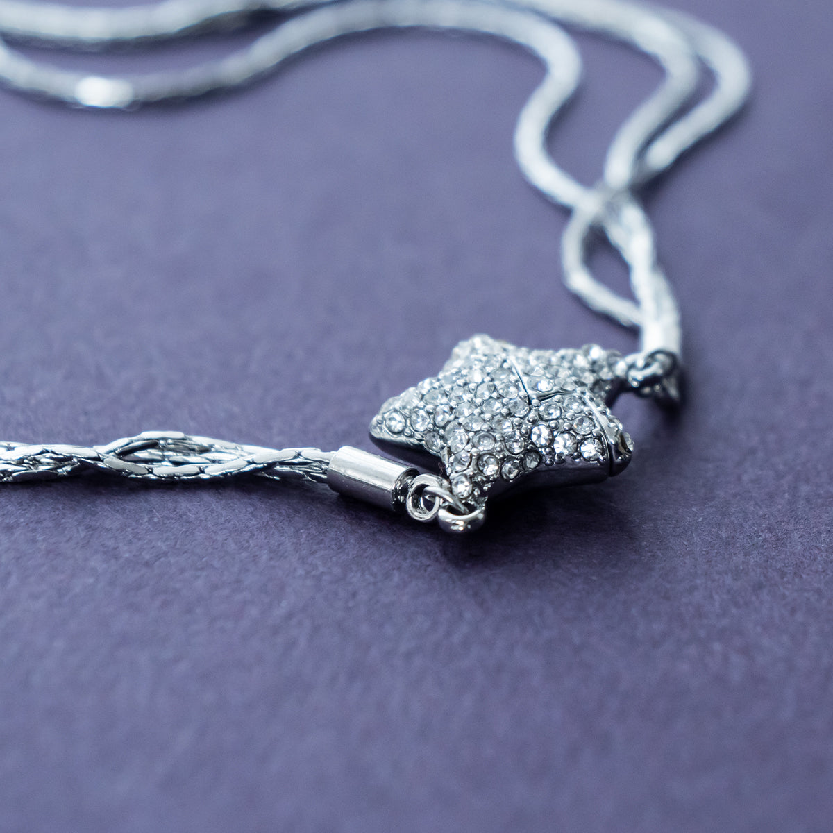 Silver necklace with a star-shaped pendant on a purple surface