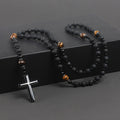 Black beaded necklace with a silver cross pendant on a dark surface