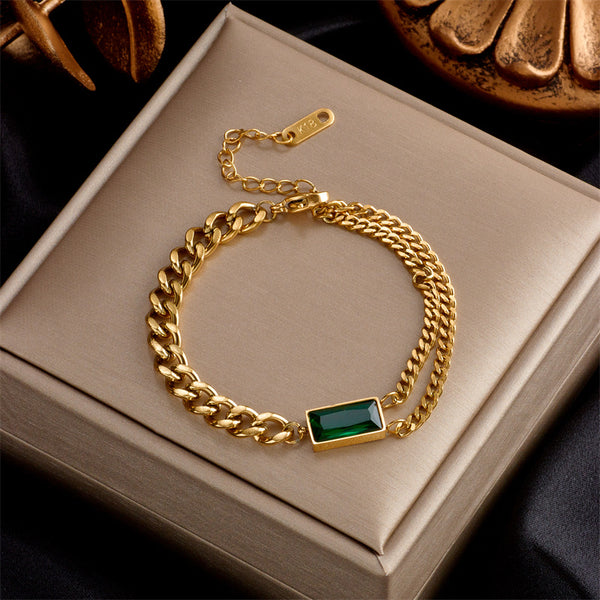 Gold chain bracelet with a green gemstone on a beige box