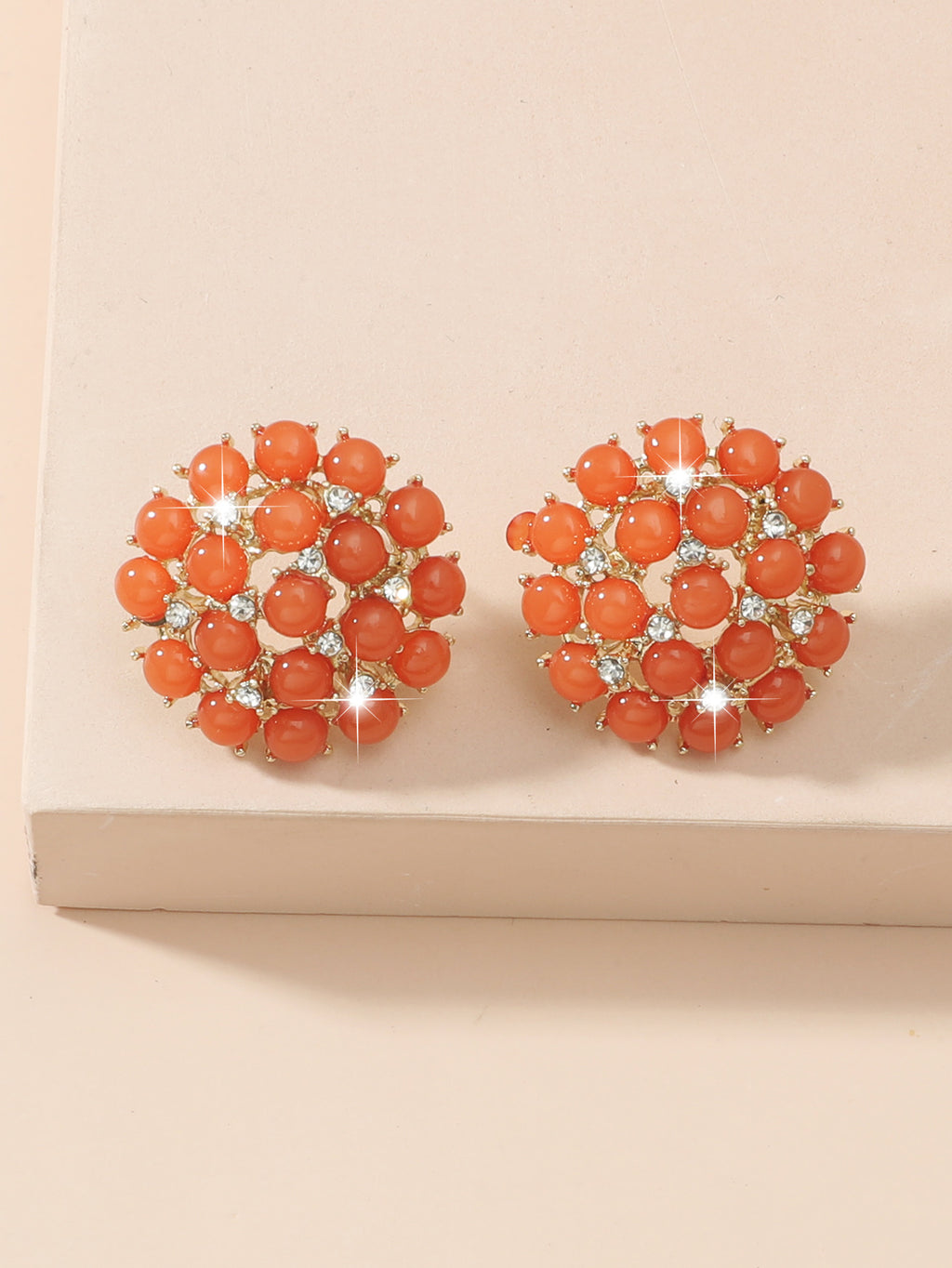 Pair of orange earrings with gemstones on a beige background