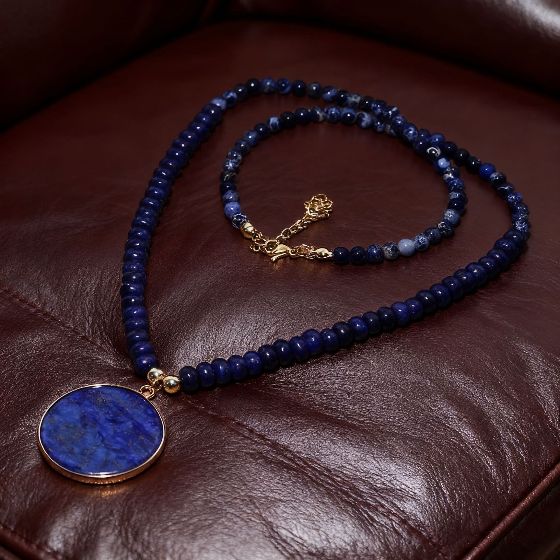 Blue beaded necklace with a gold pendant on a brown leather surface