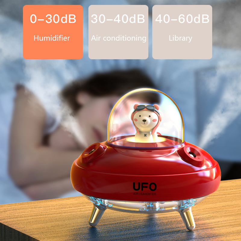 Red UFO humidifier with a bear figurine on a wooden surface, with a blurred background of a person lying down.