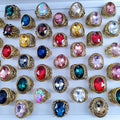 Collection of colorful gemstone rings with gold bands on a white background