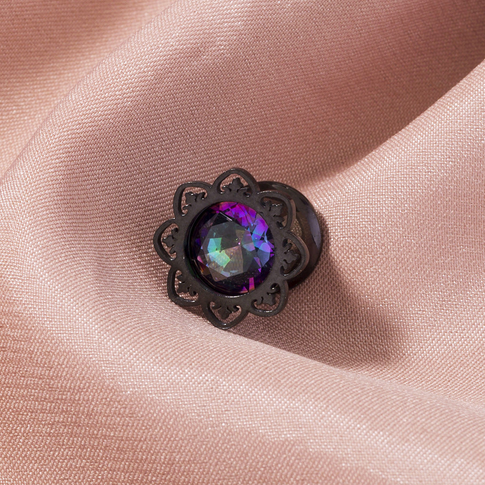 Black decorative brooch with a multicolored gemstone on pink fabric