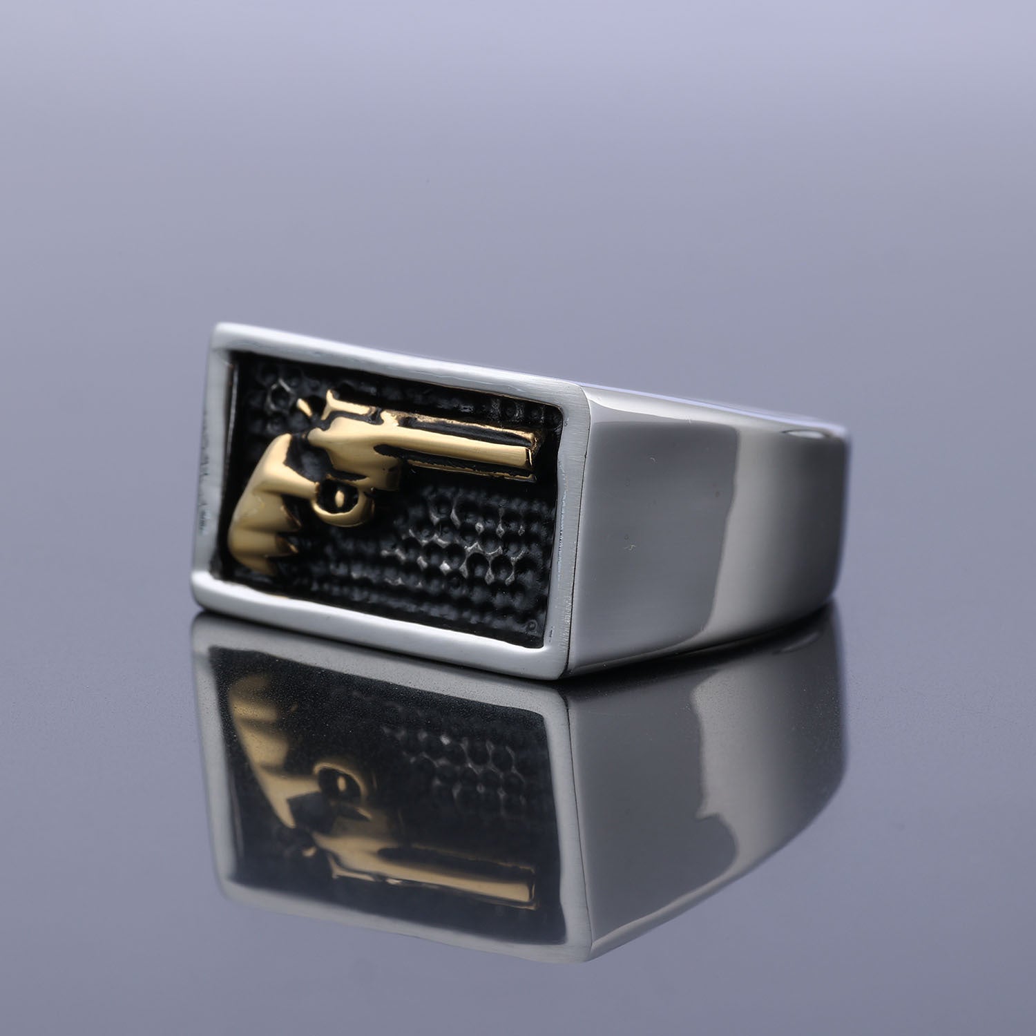 Silver ring with a gold gun design on a reflective surface