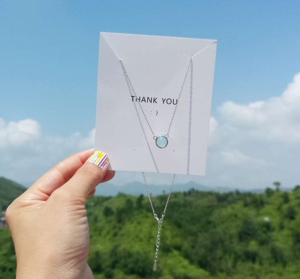 Necklace with a blue pendant held up against a scenic background