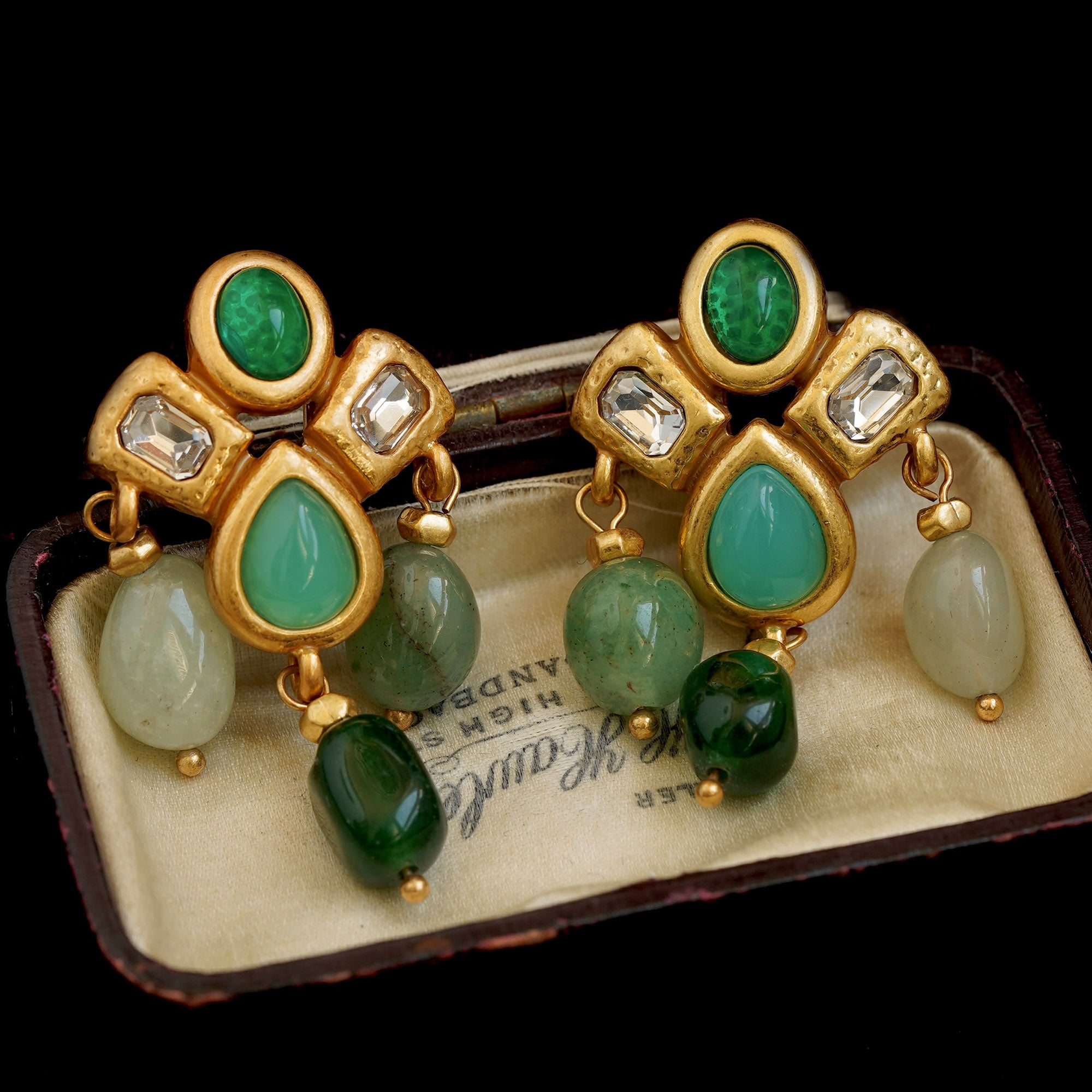 Pair of gold earrings with green gemstones on a vintage box