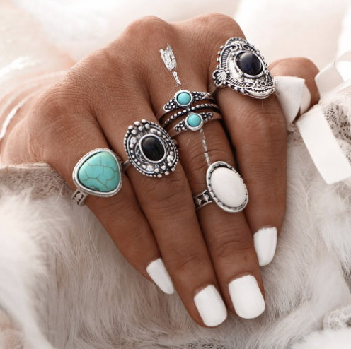 Hand wearing multiple rings with turquoise and black stones on a soft background