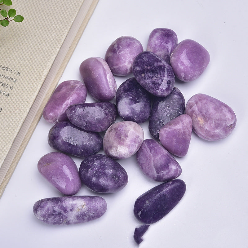 Purple stones on a white surface with a beige book and green leaves in the background