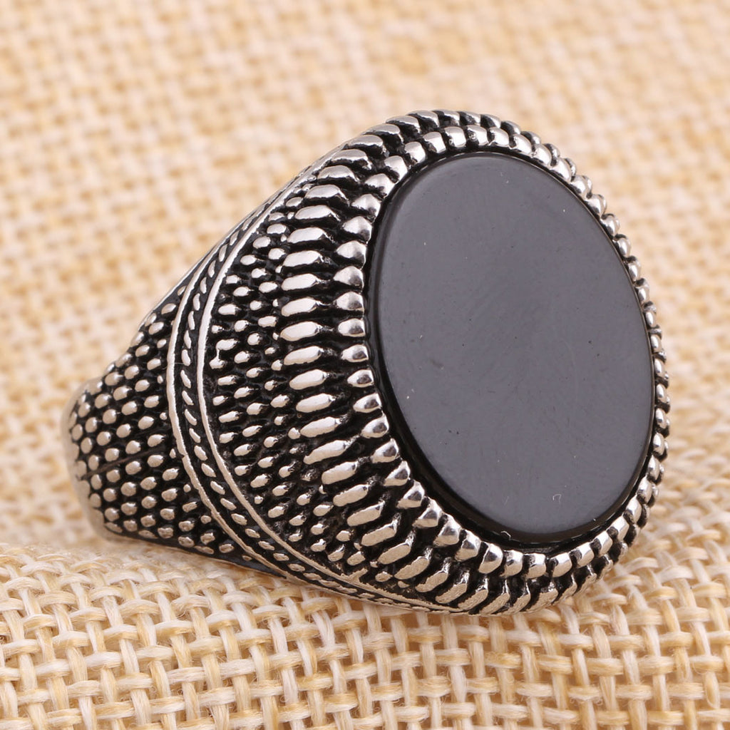 Silver ring with a black stone on a textured beige background