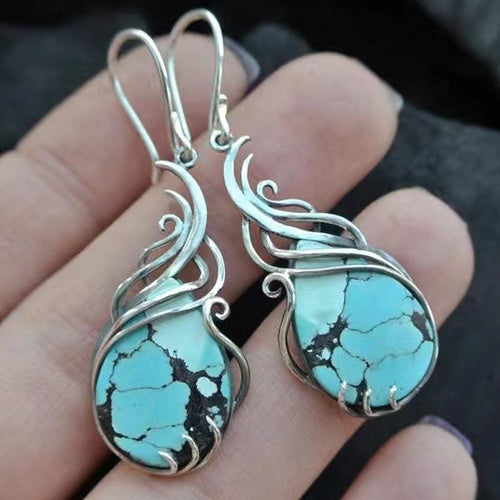 Turquoise stone earrings with silver wire wrapping held in hand against a dark background