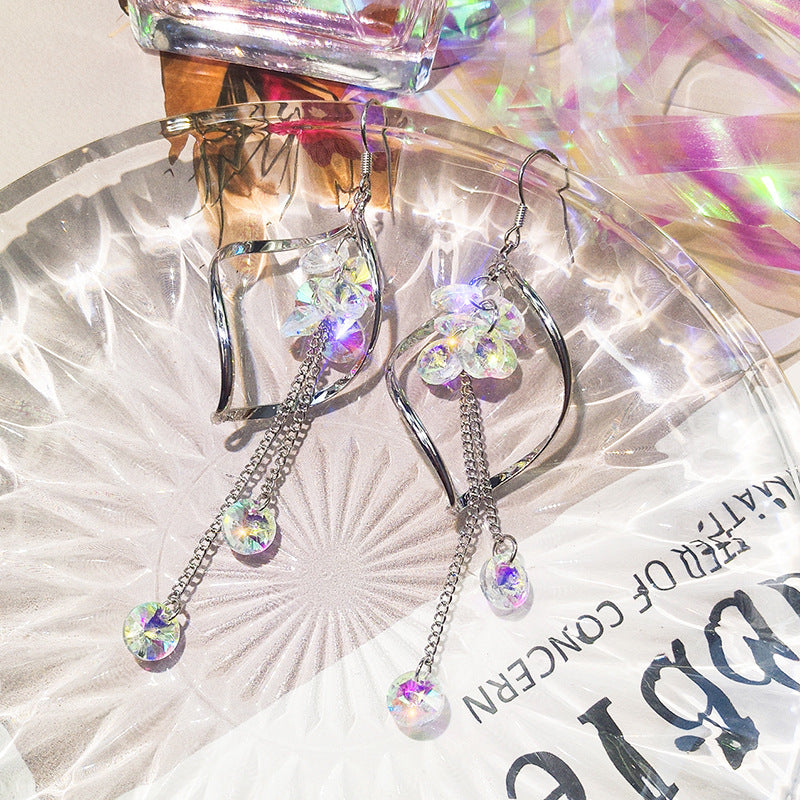 Sparkly heart-shaped earrings with chain drops on a textured surface.