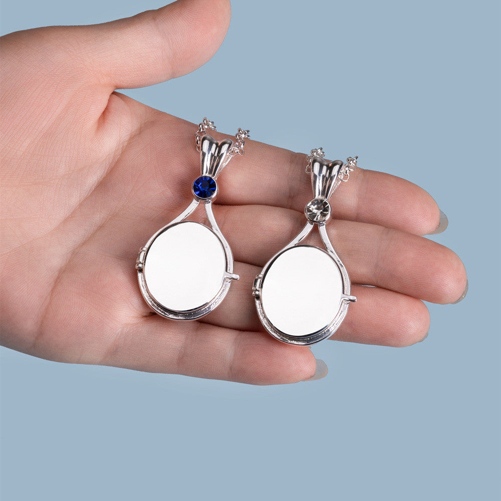 Two silver pendants with gemstones held in a hand against a light blue background
