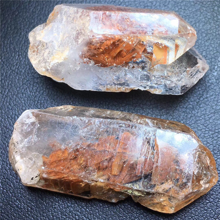 Two crystal rocks with internal mineral formations on a textured surface