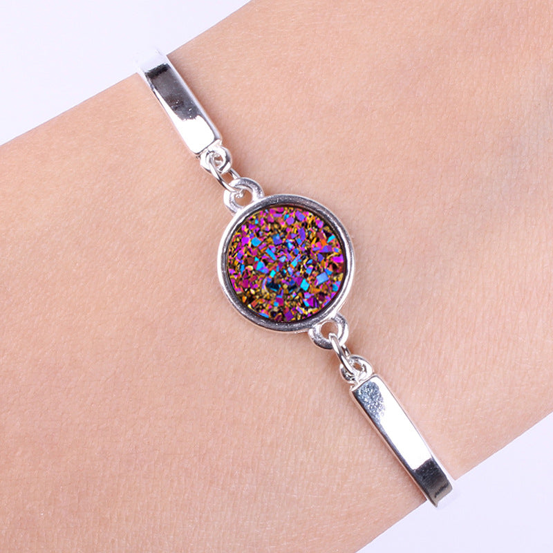 Silver bracelet with a colorful round gemstone on a wrist.