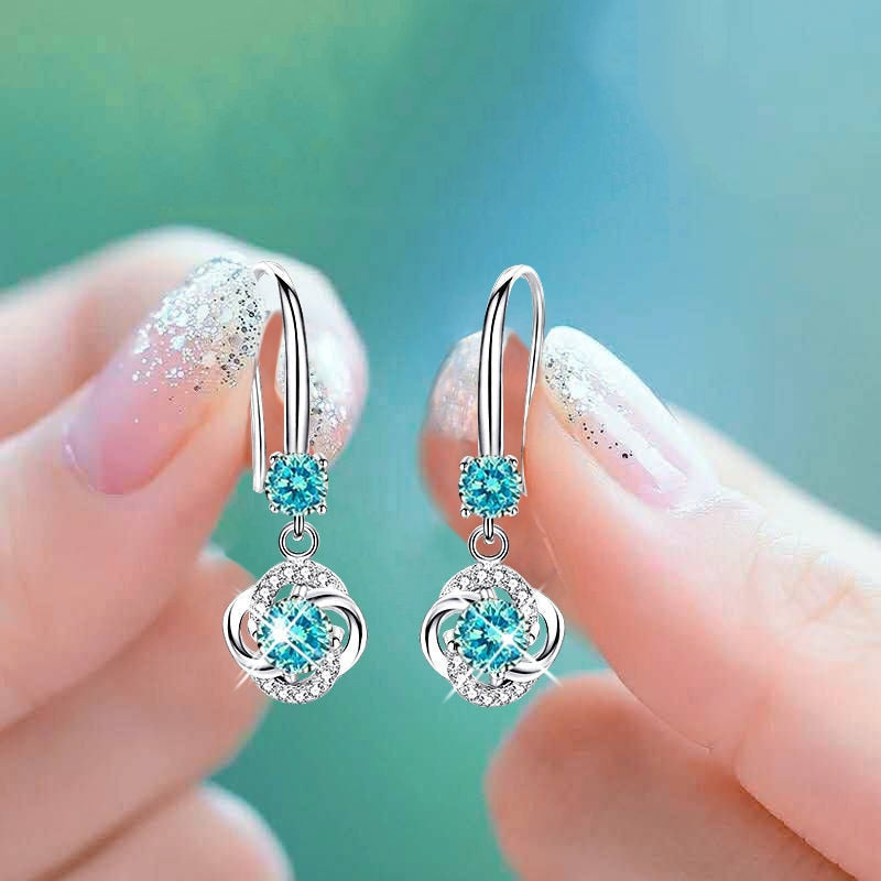 Silver earrings with blue gemstones held between fingers against a blurred green background