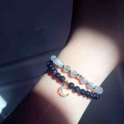 Bracelet with blue beads and moon charm on wrist against a dark background