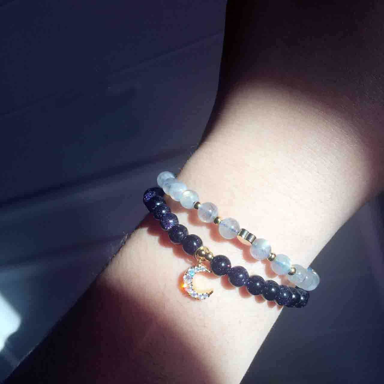 Bracelet with blue beads and moon charm on wrist against a dark background