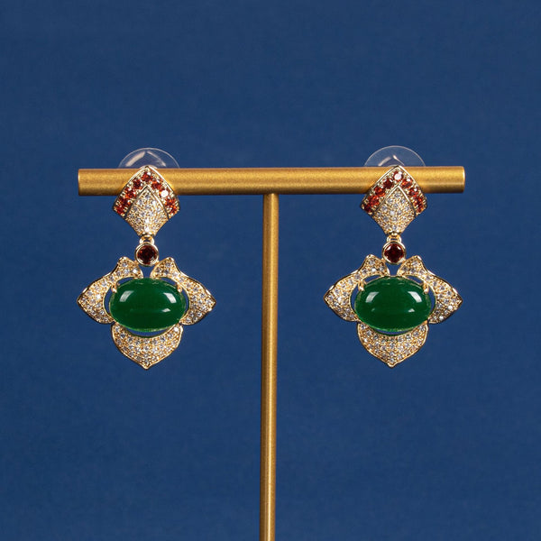 Pair of earrings with green gemstones on a gold stand against a blue background