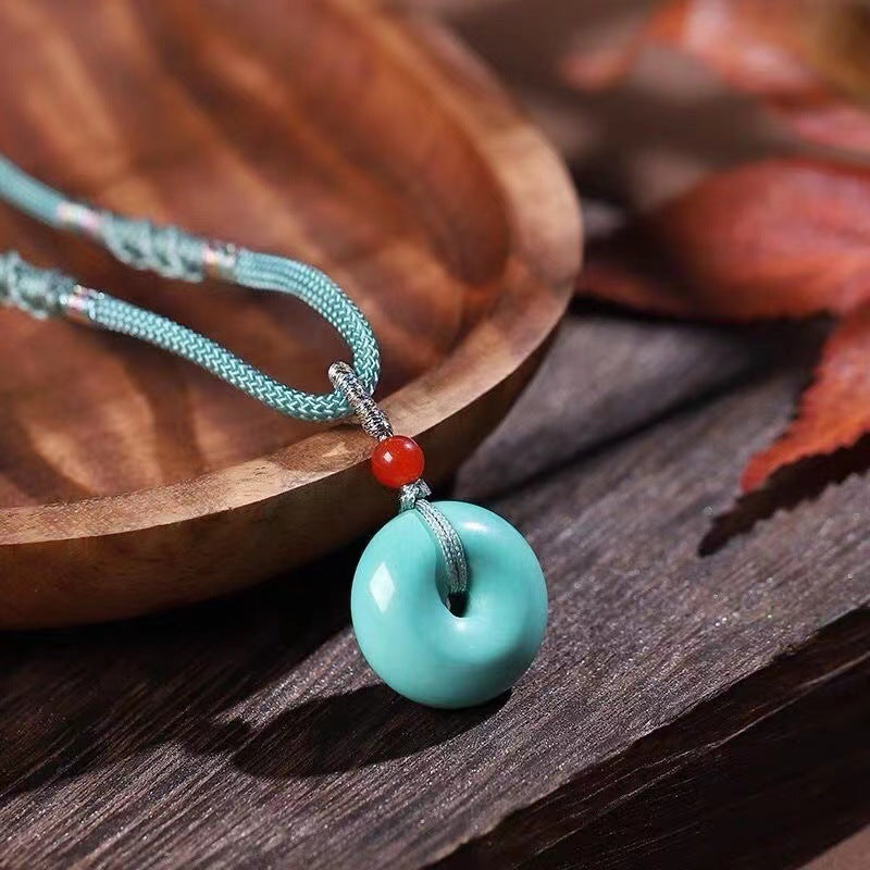 Turquoise pendant necklace with red bead on a wooden surface