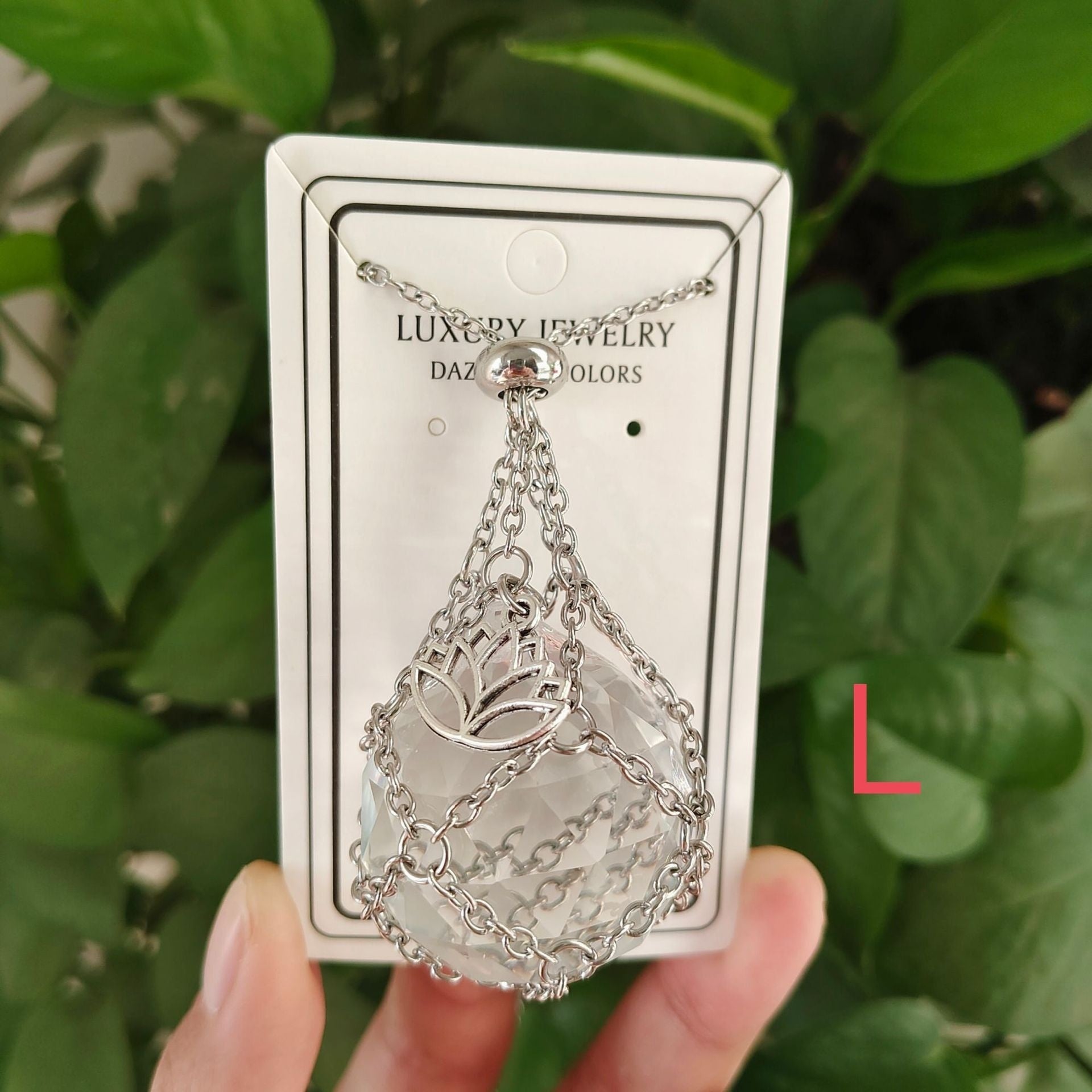Silver necklace on a 'Luxury Jewelry' card held against a green leafy background