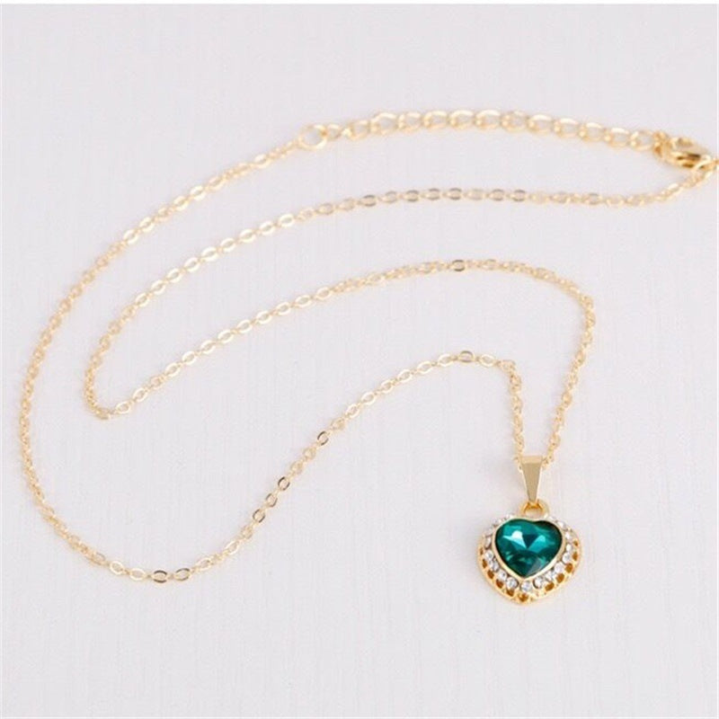 Gold necklace with a heart-shaped green gemstone pendant on a light gray background