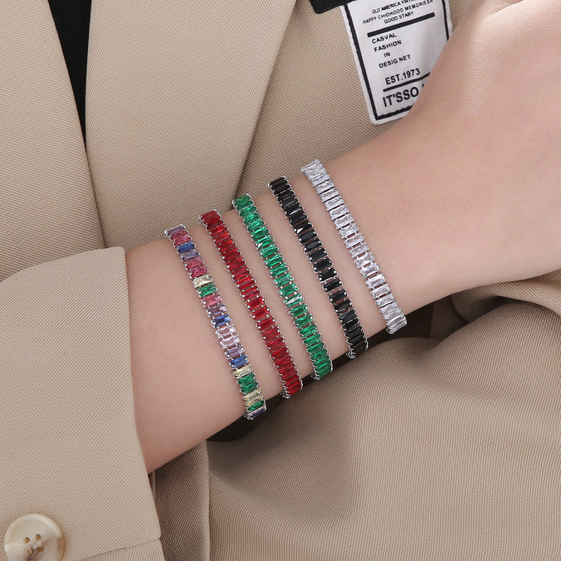 Four colorful bracelets on a person's wrist with a beige suit background