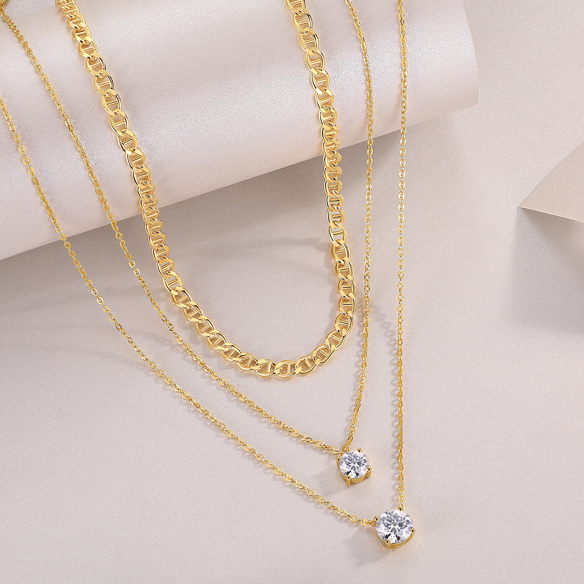 Three gold necklaces with diamond pendants on a light beige background