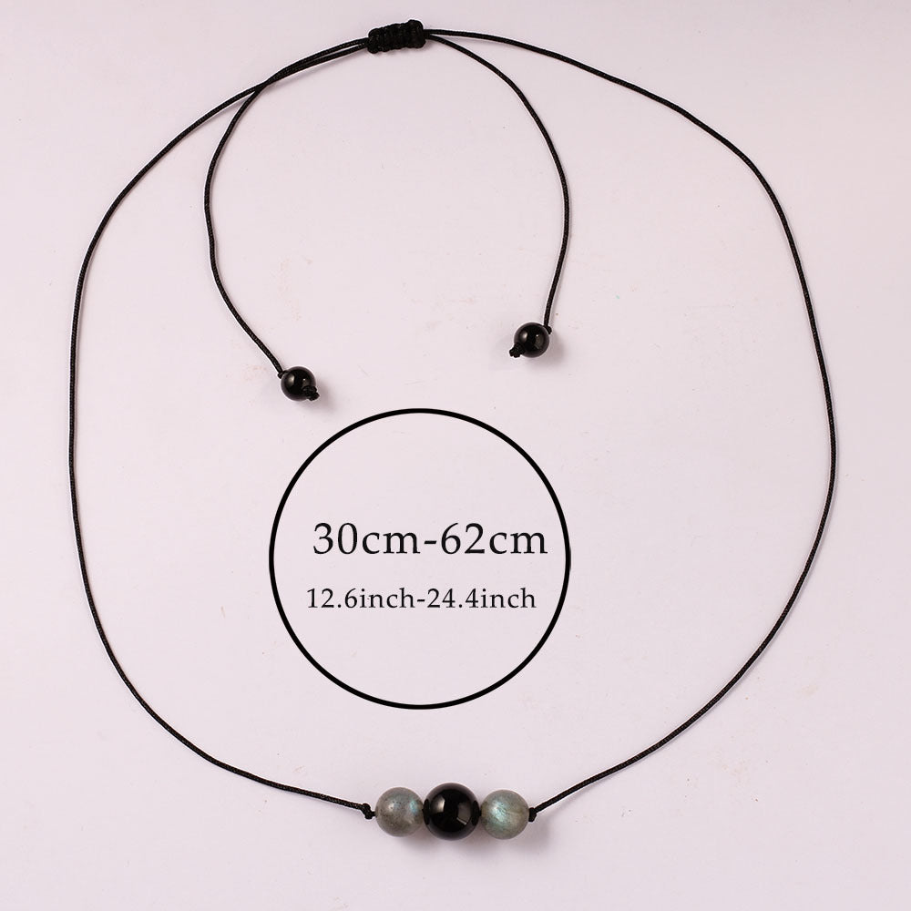 Black cord necklace with three beads on a light pink background, showing measurement range.