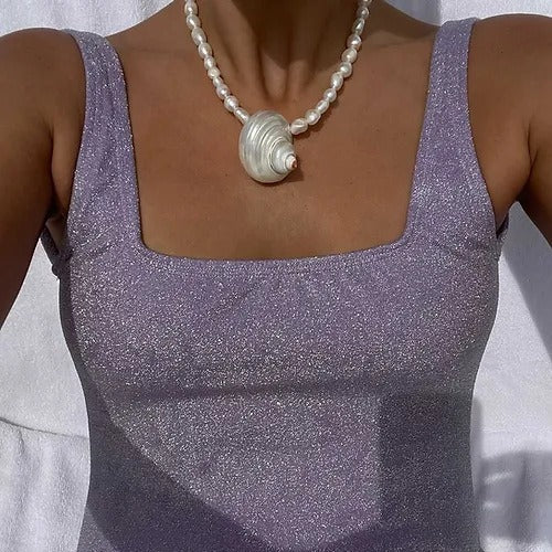 Person wearing a sparkly purple top and pearl necklace against a light background