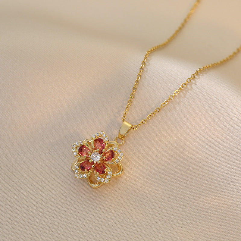 Gold necklace with a floral pendant featuring red stones and clear gemstones on a beige background