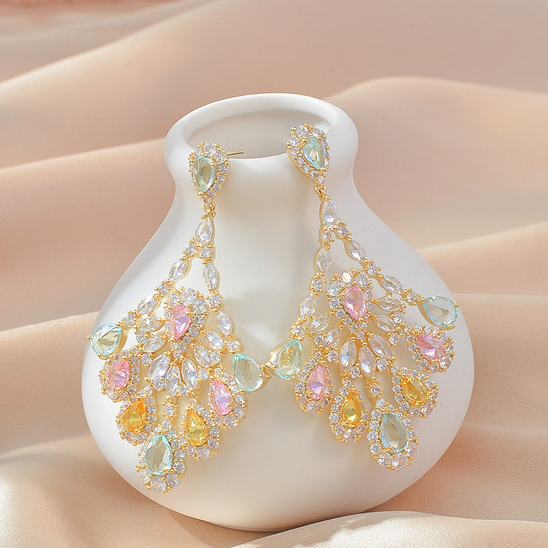 Ornate earrings with multicolored gemstones on a white vase against a beige background