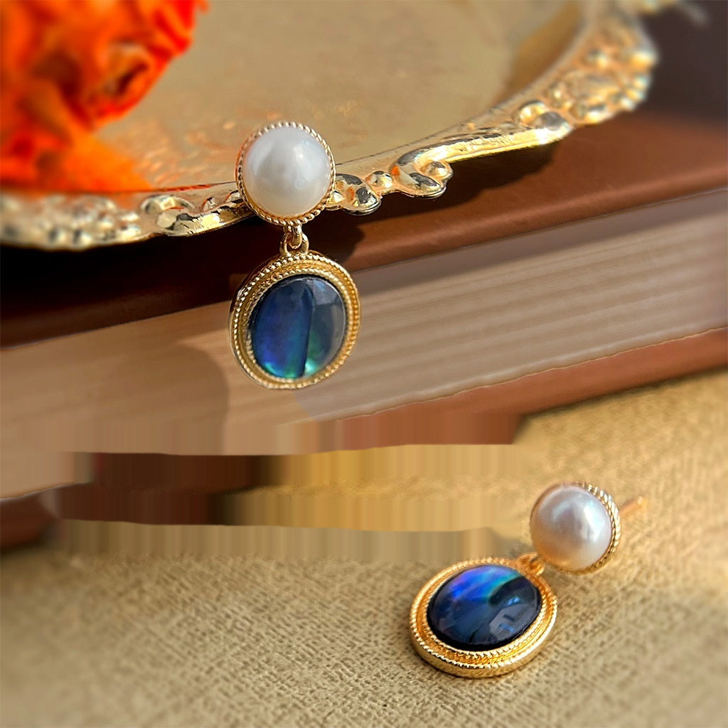 Pair of earrings with blue gemstones and pearls on a decorative stand.