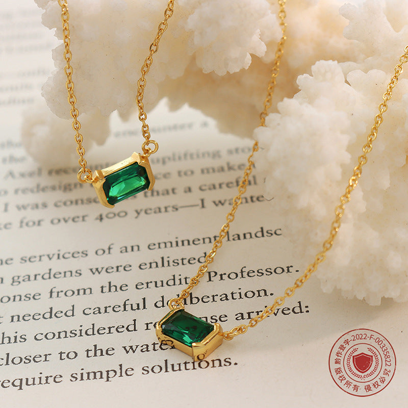 Gold necklace with green gemstones on a textured surface