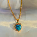 Gold necklace with a heart-shaped turquoise pendant on a white fabric background