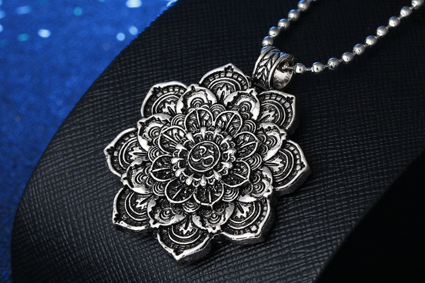 Silver mandala pendant necklace on a textured black surface with a blue fabric background