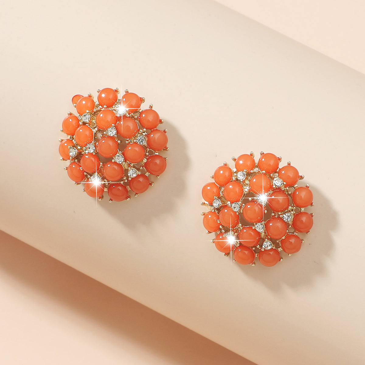 Pair of coral-colored earrings with gemstones on a beige background