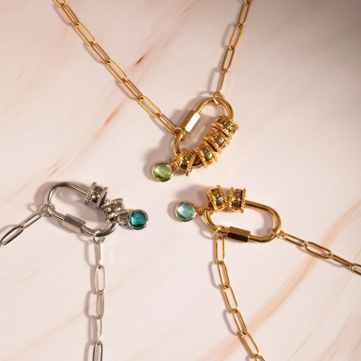 Two gold and silver chain necklaces with gemstone pendants on a light pink background