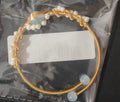 Gold bracelet with pearls and a clear stone on a white card, on a reflective surface.