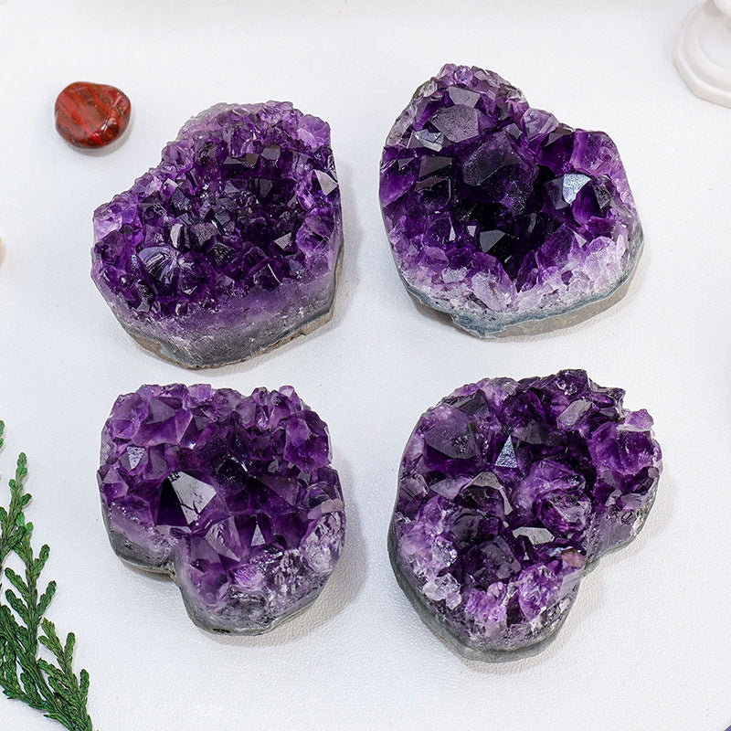 Four purple crystal geodes on a white surface with a small red stone and greenery.