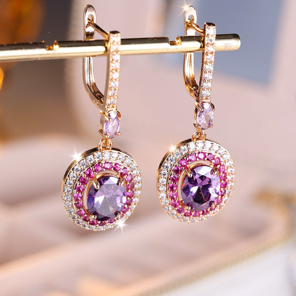 Gold earrings with purple and pink gemstones on a blurred background