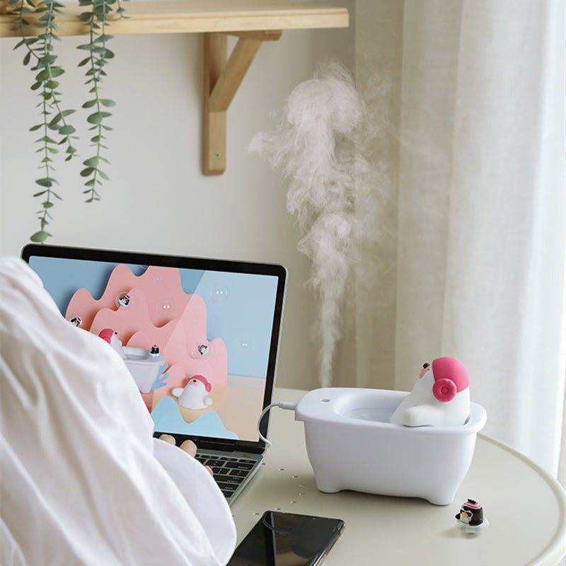 Laptop on a desk with a cartoon character on screen, next to a white humidifier with pink top.